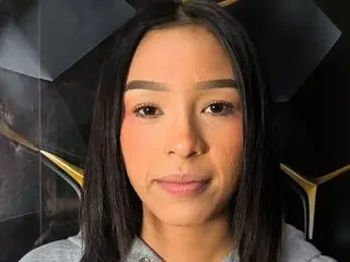 Young woman with long dark hair and natural makeup posing against a modern black geometric background.