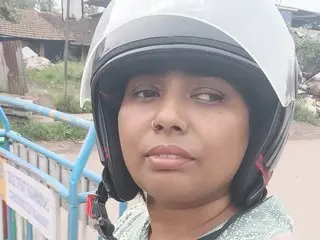 Sonia9119 wearing a white motorcycle helmet and a light green patterned top, looking directly at the camera outdoors.