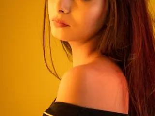 Sonikamiss — Sonikamiss poses with her long dark hair down, showing her bare shoulders and neck against a warm yellow background.