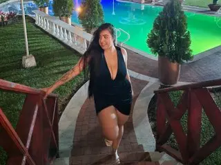 SophiRioss poses outdoors in a black bodysuit, showing off her long dark hair and bare legs while standing on a stone walkway near a swimming pool.