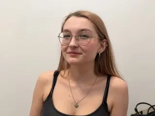 Sophie18Lux, a blonde woman wearing thin-rimmed glasses and a black tank top, looking directly at the camera against a plain white background.