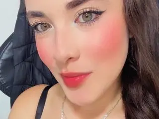 Sophie_Luxury looks into the camera with a soft smile, showing her long dark hair and makeup.