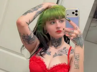 SpewkyDewky poses with her hands in her dark hair, showing off her tattoos, red lace bra, and heavy black eyeliner.