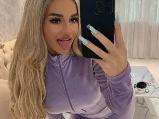 SpoilM3Mor33 takes a mirror selfie wearing a tight purple velour top, sticking her tongue out at the camera.