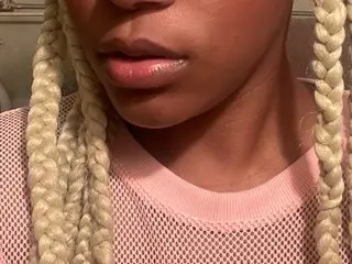 StarAct poses close up, showing her face and long blonde braids against a soft background.