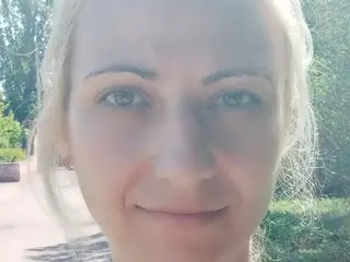 Sunbeam_Beauty looks directly at the camera with her blonde hair loose, showing her face in a close-up shot outdoors.