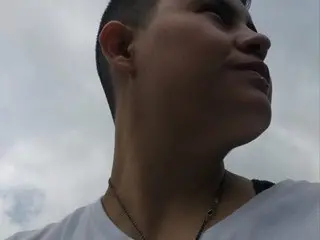 Young man in a white t-shirt looking up at a cloudy sky with a thoughtful expression.
