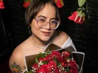 Sweet78kiara poses with her dark hair and glasses, wearing a white top and holding a large bouquet of red roses.