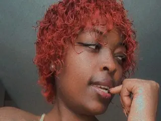 Close-up portrait of a woman with curly red hair looking thoughtful against a dark background.