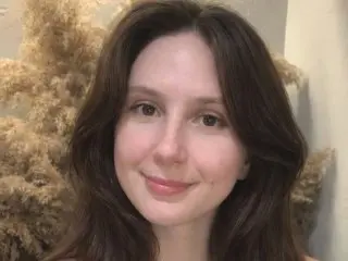 SweetLuna99 smiling at the camera with her long brown hair down in a brightly lit room.