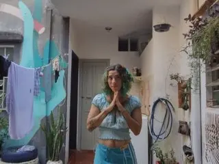 Sweet_Domi poses with her hands together in a hallway, wearing a light blue crop top and matching blue shorts.