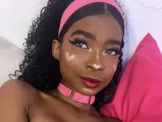 Sweetemaddy wearing a pink headband and choker, posing with dark curly hair and winged eyeliner.
