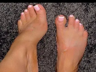 Sweetfeetlove69 shows off her bare feet and toes, held up close to the camera against a dark, textured background.