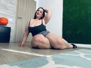SweetheartMia poses in a black tank top and patterned undies, showing off her large breasts and thick thighs while sitting on a floor.