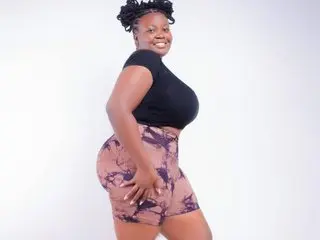 Sweetsensation19 poses in black tank top and patterned brown shorts, showing off her curves against a white background.