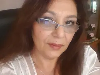 SxyVivian poses with a close-up view of her face and long brown hair, wearing a white lacy top.