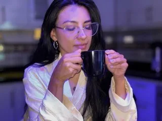 SylviaOrtega smiles while wearing a white satin robe and holding a black mug near her face.