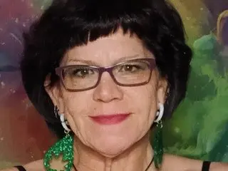 TantricToker smiles wearing glasses and a direct gaze, showing her dark hair and pink lipstick.