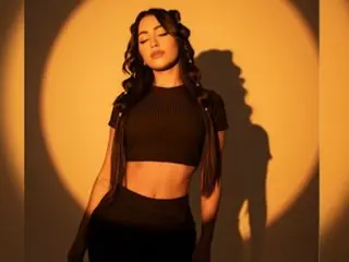 Glamorous woman in a black crop top and gloves posing against a warm golden spotlight background.