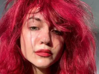 TatianaRomanova shows her face and red hair in a close-up headshot against a dark background.