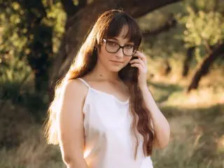 TessaDoll wearing glasses and a white tank top poses outdoors in the sunlight.