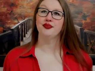 TexasHoney poses with long brown hair and red lipstick, wearing a red button-down shirt against a warm, blurred background.
