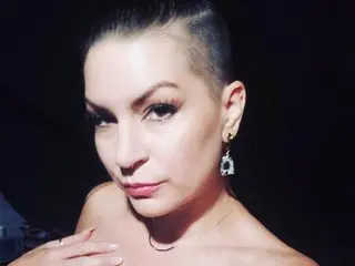 TheLadyKatrina poses close-up, showing her face, dark hair pulled back, and bare shoulders against a dark background.
