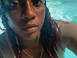 TheNaturalGoddess poses close-up in a pool, showing her face and shoulders while wearing a light-colored top.