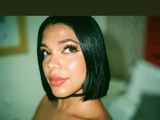 TiianaGlow poses close-up, showing her face and dark bob-cut hair with a soft glow on her skin.