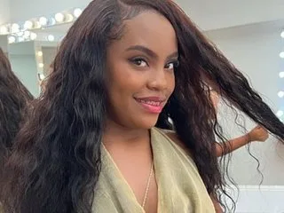 Tiifany_Baker smiles while posing with her long, wavy dark hair draped over her shoulders.
