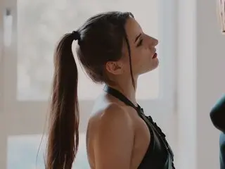 TooSweetGirl poses in profile, showing her long brown hair in a ponytail and wearing a black halter-style top.