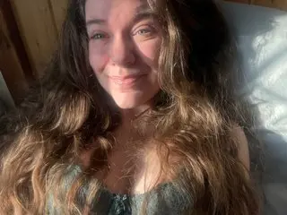 Trixieiris smiles while lying back with her long, wavy brown hair spread out around her shoulders.