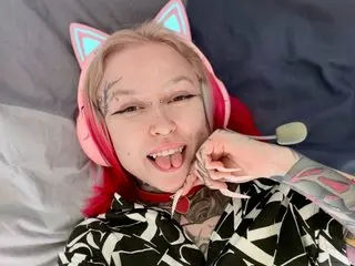 UrAlexis poses close-up, sticking her tongue out while wearing pink cat-ear headphones and a black and white patterned top.