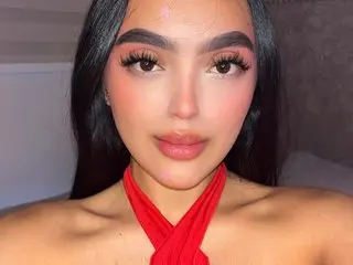 Young woman with glam makeup wearing a red halter top in a soft indoor setting.