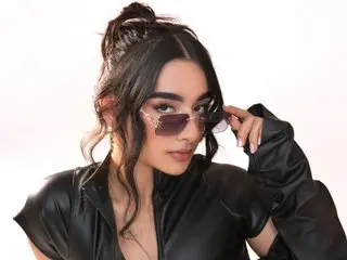 Stylish woman in a black leather jacket and tinted sunglasses posing against a white background.