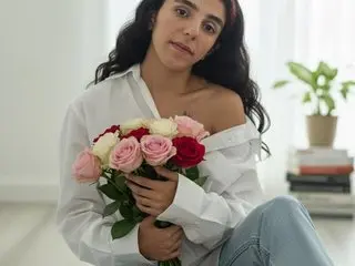 Young woman in white shirt holding a bouquet of pink and red roses in a bright, minimalist room.