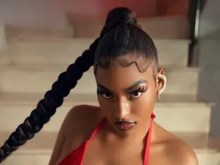 ValeriaGallardoPv poses with her dark hair in a long braid, wearing a red top while sitting on light-colored stairs.
