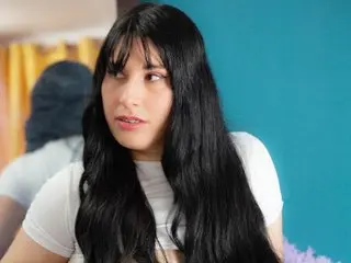 Valeriasquirt25 has long black hair and is wearing a white t-shirt against a blue background.