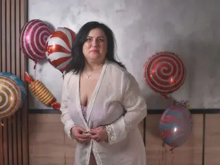 ValerieSmiths poses in a white open-front top, showing cleavage, with her dark hair down against a plain wall background.