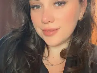 Valeriiee_xx looks at the camera with long dark hair and a soft smile, wearing a black top in a close-up shot.