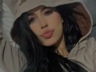 ValeryHanze poses with long black hair and a soft pout, wearing a tan hooded sweatshirt in a close-up shot.