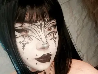 Vampkty_R poses with black hair and intricate black face paint designs over her pale skin.