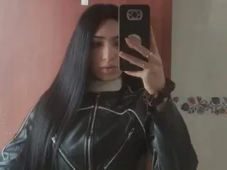 VanessaGoldXVIP poses for a mirror selfie wearing a black leather jacket and a white top, letting her long dark hair hang down over her shoulders.