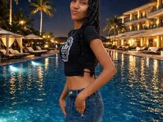 Smiling young woman in a black graphic crop top and denim shorts relaxing by a luxury resort pool at night.