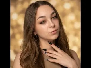 Verba poses with a soft gaze, showing her long brown hair and clear skin in a close-up headshot against a warm, blurred background.