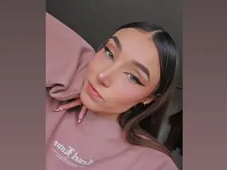 Veronicasmit111 poses close up, looking at the camera with her long brown hair down and wearing a pink sweatshirt.
