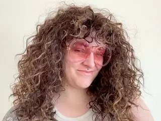 VeryVeronicaxxx poses with her long, curly brown hair and pink sunglasses, wearing a white tank top against a plain white background.