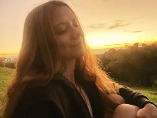 VicktoriaLou smiles with her eyes closed while sitting outdoors during a golden sunset.