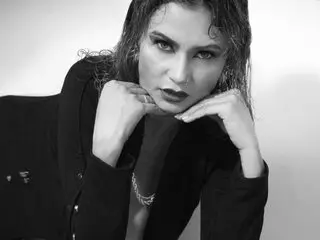 VictoriaCoperino poses with her hands near her face, wearing a black blazer and showing her dark, wet-look hair against a light background.
