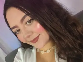 Victoriaa_24 smiles while wearing a white top and a gold necklace, showing her long dark hair and light makeup.
